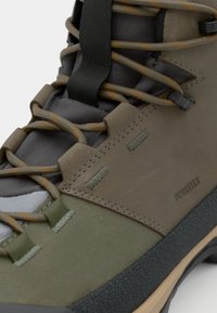 Wysokie buty trekkingowe z mieszanką szarych i zielonych materiałów, teksturowanymi powierzchniami, wzmocnionymi oczkami i solidną gumową podeszwą.