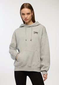 Felpa grigia con tasca a marsupio, cappuccio con cordino e dettaglio del logo in nero. Realizzata in tessuto morbido, presenta una vestibilità comoda e polsini a coste.
