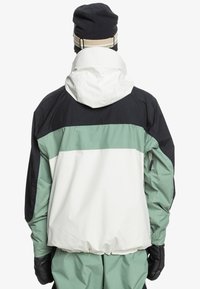 Farbblockierte Jacke mit einem weißen oberen Teil, grünem Mittelteil und schwarzen Akzenten. Verfügt über eine passgenaue Kapuze und elastische Bündchen. Das Material scheint wasserabweisend zu sein.