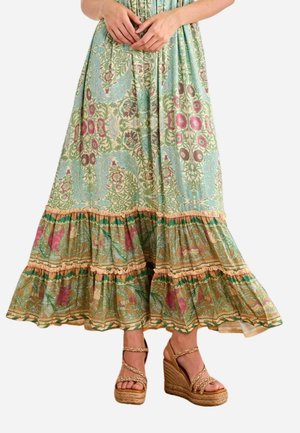 Mujer con una falda larga con estampado floral con volantes en capas y sandalias de cuña trenzadas con tiras en el tobillo.