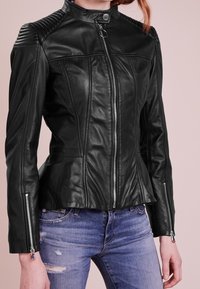 Černá kožená motocyklová bunda s přiléhavým střihem, žebrovanými rameny, dvěma předními zipy a strukturovanými detaily. Obsahuje peplum lem.