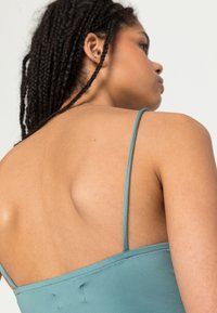 Um vestido sem mangas e sem costas, em um tecido teal suave, com alças finas, apresentando uma textura lisa e um detalhe de costura sutil ao longo das costuras.