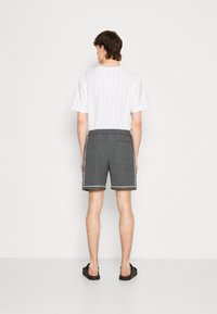 Hvit kortermet skjorte med vertikale striper, kombinert med grå stripete shorts med snor i livet og sidelommer. Svarte sandaler.