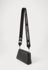 Borsa a spalla in pelle nera con forma geometrica, caratterizzata da una tracolla con logo bianco e nero e dettagli in metallo argentato.