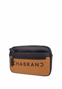 Sac en toile avec des sections noire et brune, présentant une texture lisse, une fermeture éclair sur le dessus, une poche à l’avant et un grand logo de marque en noir.