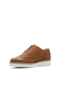 Chaussure oxford en cuir brun avec un décor de perforations et une semelle en caoutchouc blanc, vue de l'angle avant-gauche sur fond blanc.