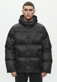 Chaqueta acolchada negra hecha de nailon brillante. Presenta una capucha, cierre frontal y paneles acolchados. Logo sutil en el pecho. Textura suave.