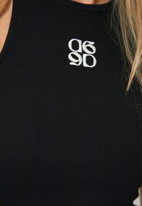 Zwarte geribbelde tanktop met een witte geborduurde grafiek met de nummers 90 en 96. De stof lijkt rekbaar en aansluitend.