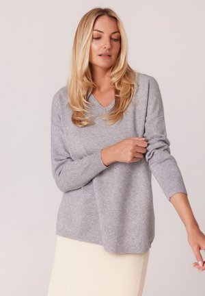 Jasnoszary sweter dzianinowy z dekoltem w kształcie litery V, prążkowanymi mankietami i dołem, charakteryzujący się luźnym krojem i miękką fakturą, zestawiony z kremową spódnicą o ciekawej fakturze.