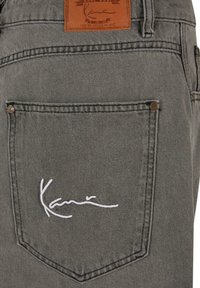 Sive traperice od trapera s kožnim zakrpom na leđima i bijelim izvezenim potpisom, s klasičnim krojem i metalnim nitnama na džepovima.