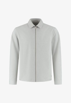 Camiseta gris claro con cremallera, cuello con solapa, mangas largas y tela texturizada sutil. Cuenta con cierre frontal de cremallera y un detalle de logo en el dobladillo.