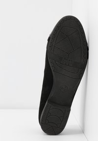 La semelle de chaussure noire présente une adhérence en caoutchouc texturé avec un motif d'arcs et de zigzags. Les bords renforcés et la marque sont visibles au bas.