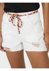 Bele čeveljske hlače iz belega denima s frayed robovi in uničenimi detajli, ki vključujejo večbarvni pleteni pas. Vidna sta dva stranska žepa.