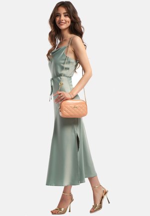 Robe en satin verte avec des bretelles spaghetti et une fente sur le côté, accompagnée d'un sac à main en pêche matelassé et de sandales dorées métalliques à lanières.
