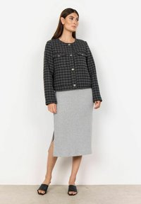 Mustat ja harmaat houndstooth-kuvioiset takki, jossa on neljä etutaskua ja hopeanvärisiä nappeja, yhdistettynä vaaleanharmaaseen ribbimittapituiseen hameeseen ja mustiin liukusandaaleihin.