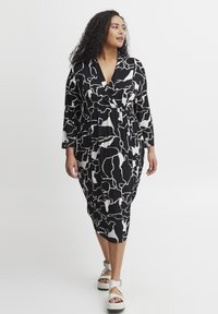 Vestido envolvente de patrón en blanco y negro con escote en V, mangas largas y cintura ceñida, combinado con sandalias de plataforma blancas con tiras.
