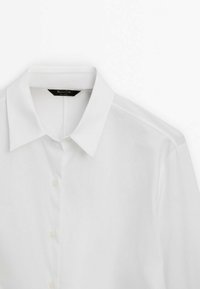 Hvid skjorte med klassisk krave, glat tekstur og fem knapper foran; etiketten viser "Massimo Dutti".