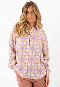 Blouse légère à motifs dans des teintes pastel de rose et de violet, dotée d'un design en grille avec des accents floraux et une fermeture à boutons.