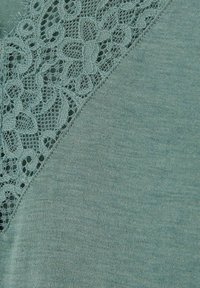 Türkises Oberteil mit V-Ausschnitt und Spitzenbesatz, aus weichem Stoff mit feiner Textur und glatter, gleichmäßiger Oberfläche.