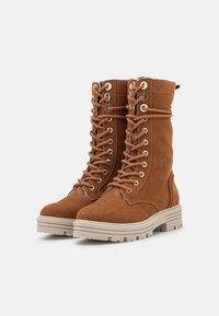 Bottes en suede marron à lacets avec œillets en métal, semelles épaisses beige et doublure intérieure douce pour plus de chaleur. Conçues pour la durabilité et le confort.