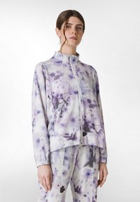Lila tie-dye zip-up jacka med hög krage, elastiska manschetter och två sidofickor, tillverkad av ett mjukt, lätt material.
