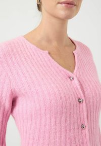 Różowy prążkowany kardigan wykonany z miękkiego materiału, z dekoltem w serek i trzema srebrzystymi guzikami z przodu. Teksturowana tkanina o delikatnym połysku.