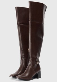 Hohe, dunkelbraune Lederstiefel mit Blockabsätzen, senkreichem Reißverschluss und einem kleinen Schnallenriemen um den Knöchel.