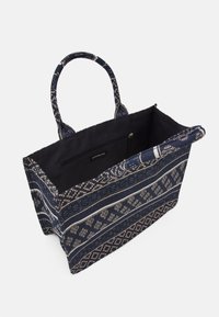 Sac fourre-tout bleu marine avec extérieur tissé à motifs, comprenant des rayures et des designs géométriques. L'intérieur comprend une poche zippée et une doublure contrastante.
