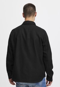 Black button-up shirt with a smooth texture and curved hem, featuring long sleeves and a classic collar.