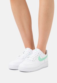 Valkoiset nahkaiset tennarit, joissa vihreä Nike-swoosh, rei'itetty kärki ja kuvioitu kumipohja. Nauhallinen malli, jossa pehmustettu varsi.