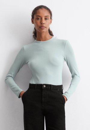 Hellblaues Langarmshirt mit geripptem Schnitt, runder Ausschnitt und taillierter Passform, kombiniert mit schwarzen hochgeschnittenen Jeans.