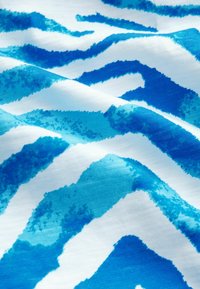 Textil med ett vågigt mönster i blått och vitt, där olika nyanser av blått skapar en texturerad, akvarelleffekt över tyget.