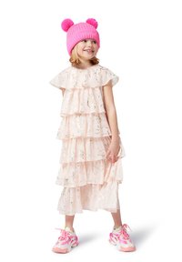 Lagdelte rosa kjole med volangermer, prydet med delikate sølvmønstre. Båret med en lys rosa strikket hatt og fargerike joggesko.