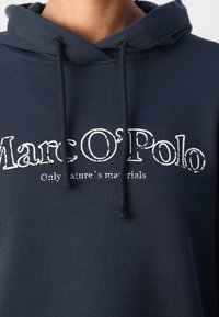 Sweat à capuche bleu marine avec cordons, avec texte blanc "Marc O'Polo" et un slogan plus petit "Only nature's materials" sur la poitrine.