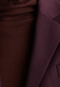 Närbild av en mörkpurpur blazerlapel över en vinröd ribbad tröja.