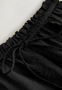 Fekete szoknya fodros derékkal és zsinórral. Az anyaga textúrált megjelenésű, lágy, matt felülettel.