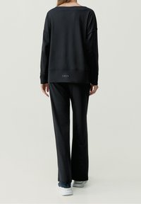 Czarny, miękki zestaw wypoczynkowy z luźną bluzą i dopasowanymi spodniami, oba o swobodnym kroju i subtelnych detalach designu.