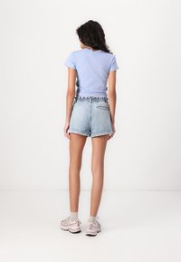 T-shirt aderente azzurro chiaro, pantaloni shorts in denim con orlo sfrangiato e cintura elastica, e scarpe sportive beige con accenti grigi.