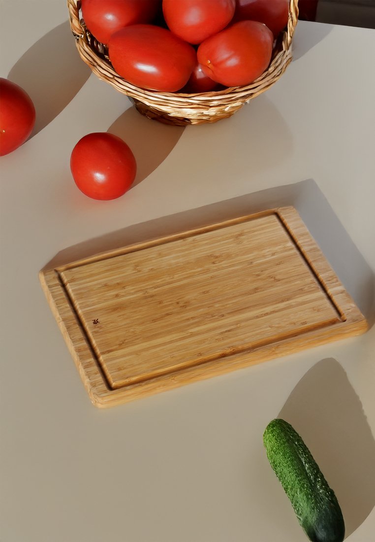 Cesto di vimini pieno di pomodori rossi, pomodori sciolti nelle vicinanze, un tagliere di legno e un cetriolo su una superficie beige.