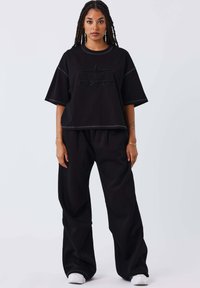 T-shirt nera oversize con logo "PXP" ricamato, abbinata a pantaloni neri larghi, entrambi realizzati in tessuto morbido e testurizzato.