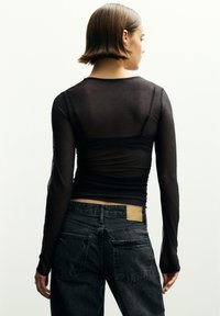 Fekete, hosszú ujjú, áttetsző felső texturált mintával és pöttyökkel. Magas derekú fekete farmernadrággal párosítva, amelyen barna bőr címke található.