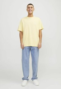 T-shirt in cotone giallo a maniche corte con logo bianco, abbinato a jeans dritti blu chiaro e sneakers bianche.