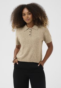 Beige, rövidujjú kötött polo pulóver, klasszikus gallérral, három fekete gomb díszítéssel és puha textúrával. Fekete nadrággal párosítva.