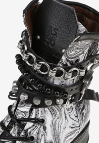 Bota de cuero marmoleado en blanco y negro con tachuelas metálicas y cadenas, que presenta un diseño de cordones y un collar acolchado para mayor comodidad.