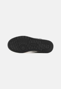 Semelle de chaussure en caoutchouc noir avec motifs de grip texturés et logo Lacoste embossé au centre.