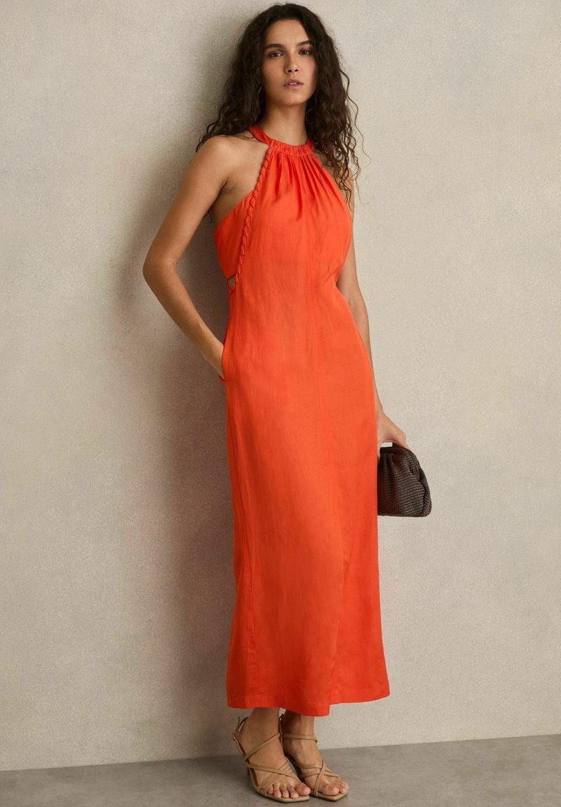 Langes oranges Kleid mit Neckholder, gerafftem Design und Seitentaschen, kombiniert mit beigen Riemchensandalen und einer kleinen strukturierten braunen Tasche.