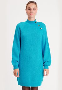 Türkises Strickkleid mit hohem Kragen, langen Puffärmeln, gerippter Textur und drei dekorativen goldenen Knöpfen an der Schulter.