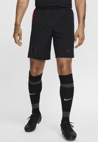 Sorte træningsshorts med røde og blå sideindlæg, udstyret med et logo-patch og parret med sorte sokker med grå striber og fodboldstøvler.