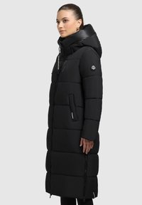 Sort dunjakke med lang pasform, brede vandret quiltede sektioner, oversized hætte, sidelommer og lynlåsdetaljer.