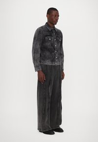 Jachetă din denim de culoare neagră estompată, cu un finisaj texturat, având buzunare frontale și nasturi metalici. Asortată cu pantaloni din denim lejeri, de aceeași culoare.